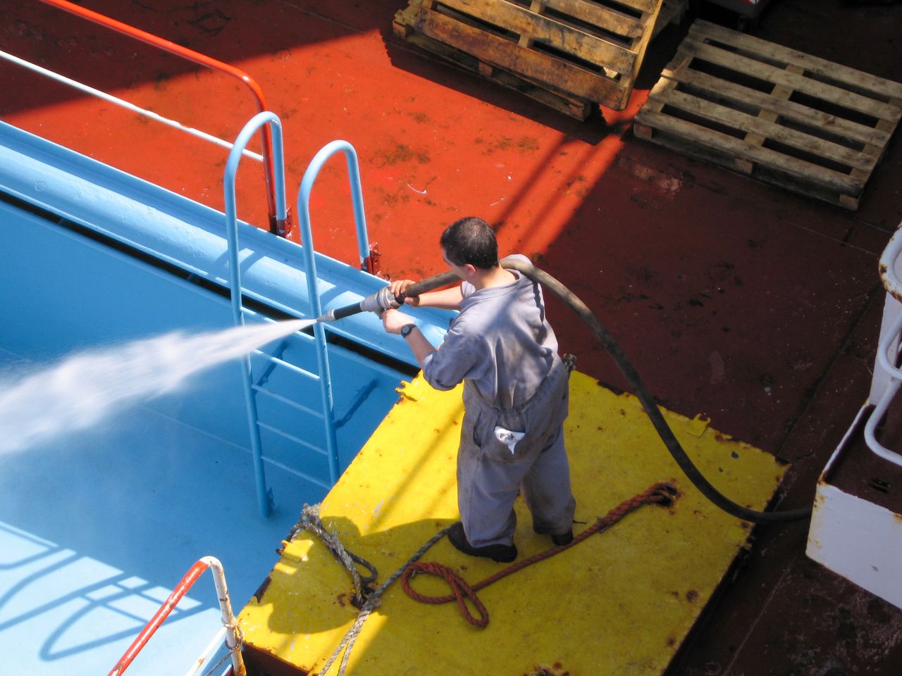 mobile-01 A worker using a high-pressure hose to clean the deck of a ship, showing industrial processes.