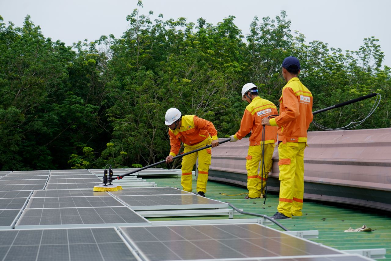 Services-01 Three technicians in uniforms and hardhats clean rooftop solar panels in a renewable energy project.